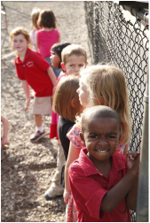 Children outside in a line standing  by a chain link fence